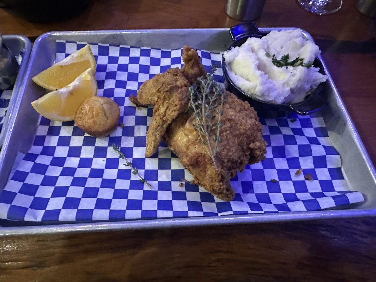Garnished fried chicken with a bowl of mashed potatoes, two slices of lemon, and a jalapeño muffin.