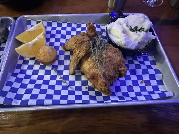 Garnished fried chicken with a bowl of mashed potatoes, two slices of lemon, and a jalapeño muffin.