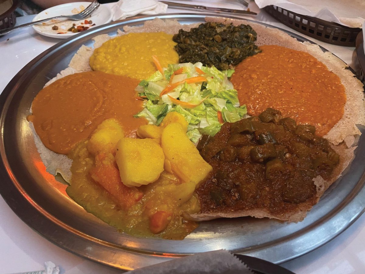 An array of curries resting on injera on top of a silver platter