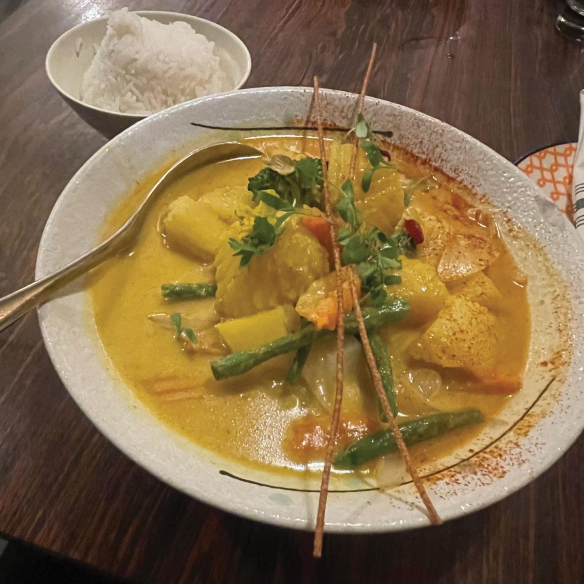 Bright yellow curry garnished with green beans and sprouts.