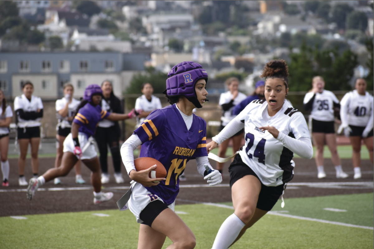 Quarterback Nicole Hayeems '26 runs the football down the field, avoiding an opposing Sequoia player who wants to grab her flag, at a home game. 