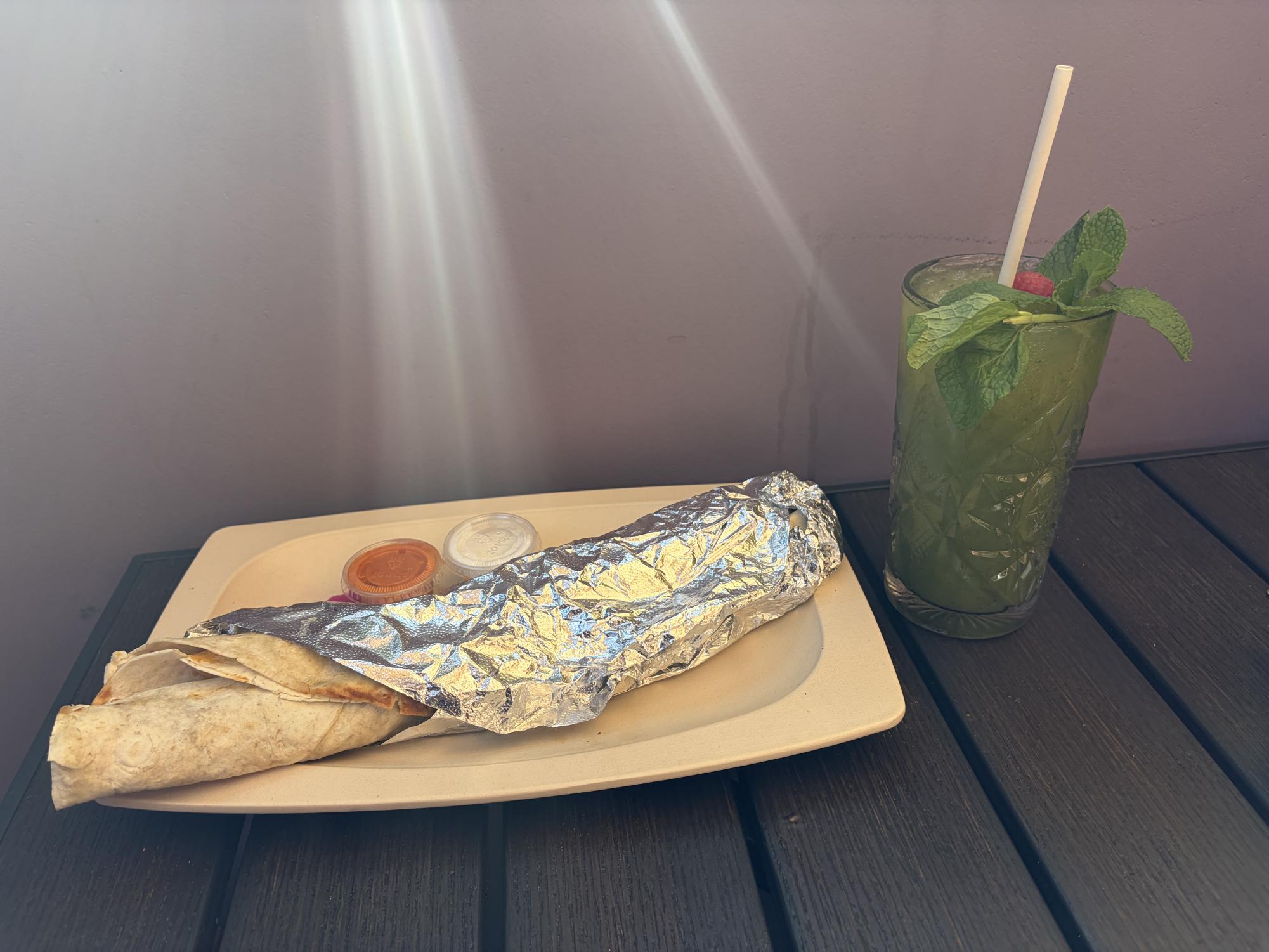 A shawarma wrapped in tin foil with dipping sauce and mint lemonade.